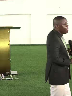 The cover image shows a man giving a speech in what appears to be a church. He is wearing a black suit with a white shirt and a green and white striped tie. He is holding a microphone in his right hand. Behind him appears to be a fake turf floor.