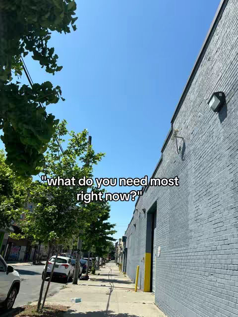 An outdoor scene on a sunny day with a tree on the left side, a building on the right, and a sidewalk and parked cars in the middle. The sky is blue. Text is overlaid on the image.