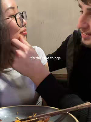 A man is gently touching a woman's face as they look at each other, with a dining table setting visible, creating a romantic ambiance.