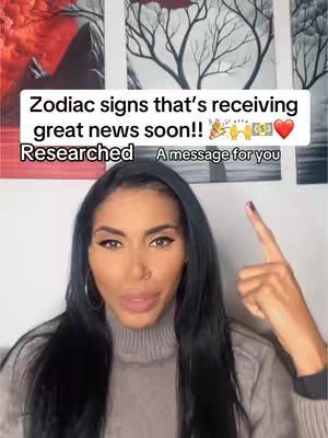 A woman with long black hair is centered in the frame, pointing upwards with her right index finger. Above her, a white rectangular bar contains the text: "Zodiac signs that's receiving great news soon!!" The background features three framed artworks of a similar style, with the top two frames appearing to be a painting of leafless tree branches. The overall aesthetic is simple yet engaging.