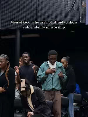 A group of people appear to be in a church setting. The shot is a medium view. The background is dark and blurred. The focus is on the people, some with hands raised in worship. A text overlay in the image reads, 'Men of God who are not afraid to show vulnerability in worship.'