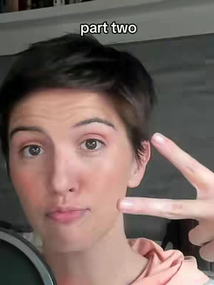 A close-up shot of a person with short dark hair, looking directly at the camera. The person is making a peace sign with their hand near their face, and the text "part two" appears at the top of the frame. The background is blurred, likely from a room.
