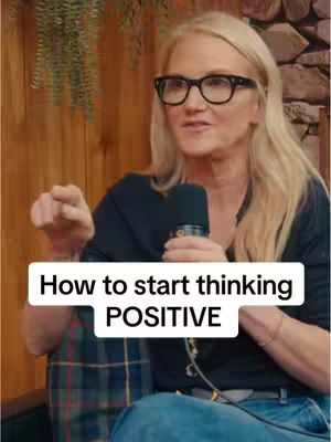 A woman with blonde hair and glasses is speaking into a microphone, with overlaid text about positive thinking. The background includes wood paneling and greenery.