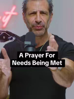 The cover image shows a man in a dark shirt, centered, with his hands up and out, palms forward, as if in a gesture of openness or presenting something. He has short hair and a beard, and a microphone is positioned in front of him. The background is blurred, featuring a glowing neon sign. Text overlaid on a black bar across the image reads, 'A Prayer For Needs Being Met'.