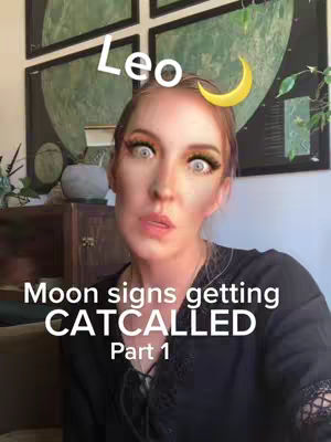 A woman with light skin and red hair is the primary focus, appearing in a close-up shot against an indoor background. She's wearing a dark top and has a slightly surprised, expressive face with wide eyes due to a filter. Above her head are the word "Leo" in a white font and a yellow crescent moon graphic, suggesting astrology. The background has a framed artwork that appears to be a green landscape.