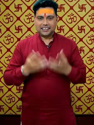 A man in a red shirt with a tilak on his forehead poses in front of a yellow background with repeating patterns.