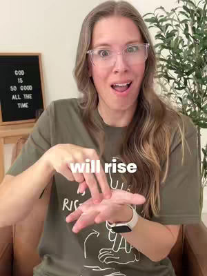 A woman with long, light brown hair and glasses looks directly at the camera with an open mouth and surprised expression. She is wearing a green t-shirt and gesturing with her hands, with text "will rise" overlaid on the image.