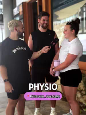 The image captures three individuals in a casual outdoor setting, likely for an interview. The man on the left is holding a microphone towards the woman on the right, who holds a pink tumbler. The middle man is also holding a microphone. Below the subjects, there is a text overlay with the words 'Physio' and 'Brisbane, Australia' in a colored banner.