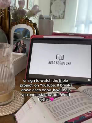 A person is studying the bible and a tablet that says "READ SCRIPTURE" with a bible open in front of them. The scene is of a desk with decoration.