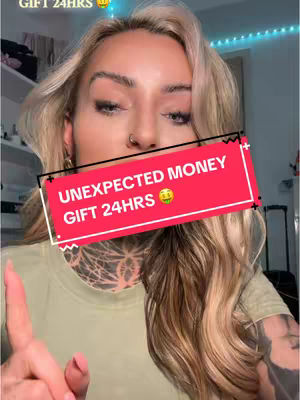 A woman with long wavy blonde hair is centered in the frame, looking towards the viewer with a serious expression. A red banner with white text stating 'UNEXPECTED MONEY GIFT 24HRS', along with a money bag emoji covering the bottom of her face. She's wearing a light green shirt and has hand tattoos. The background, though blurred, suggests a room with a shelf and a curtain of blue lights.