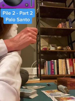 The cover image shows a person's hand, partially visible, interacting with a stack of tarot cards. A shelf with books and other objects is placed in the background. A blue text box at the top displays 'Pile 2 - Part 2 Palo Santo'. The composition seems to center around the ritual or practice of tarot reading.