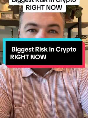 A selfie-style shot focused on a man's face and upper chest. He is wearing a pink and white striped collared shirt. The background is slightly blurred and shows an interior setting with shelves and objects. Overlaid on the image is a black rectangle with the text: "Biggest Risk In Crypto RIGHT NOW".