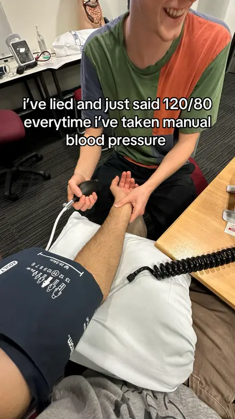 The image shows two people in what appears to be a medical setting. One person, who is wearing a multi-colored shirt, is smiling and positioned to the right. In the foreground, another person has their arm extended, and a blood pressure cuff is wrapped around it. The person in the foreground is holding a sphygmomanometer. The setting includes medical equipment and a plain background. The text overlay across the image indicates the video's content.