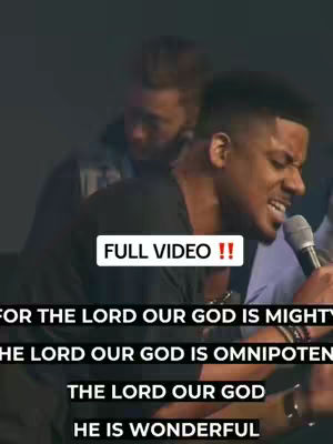 The image shows two men; one is the focal point, singing into a microphone amidst a performance setting, while another is slightly blurred in the background. Text overlays indicate the video is a full one with phrases from a worship song.