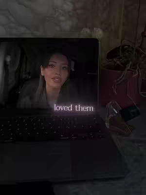 A laptop displays a video featuring a woman with long hair, looking into the camera. The overlay text reads 'loved them' in a soft, purple font. Besides the laptop, there's a small decorative object, and the background suggests a cozy, indoor setting.