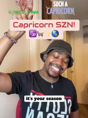 A smiling Black man wearing a black bucket hat and a black t-shirt. The cover image has text elements related to Capricorn season and astrology. The man is holding one hand up with a drawing. His other arm had a bracelet. The background is blurred, showing a room.