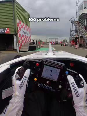 An interior view from inside a race car, showing the driver's hands on the steering wheel and a view of the track ahead. A text overlay reads '100 problems'.