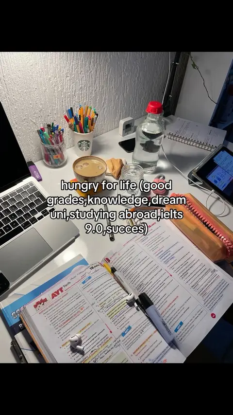 A desk covered with school supplies, including books, pens, a laptop, and a cup of coffee. The image is of a well-lit scene, with a bottle of water visible. Overlay text provides additional context.