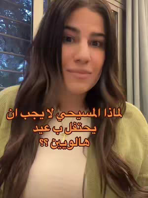 A woman with long brown hair, a white top and a green sweater looks at the camera, with text overlayed. A curtain is behind her to the right, with a window with a blurred outdoor view to her left.