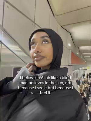 A woman wearing a black hijab and coat looks upwards with a thoughtful expression in a brightly lit hallway. Text overlays the image.