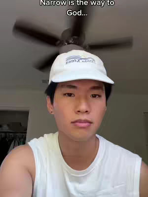 A young man with dark hair and a white baseball cap is centered in the frame, looking directly at the camera with a neutral expression. Above him, the text overlay reads, 'Narrow is the way to God...'. A ceiling fan is visible in the blurred background.