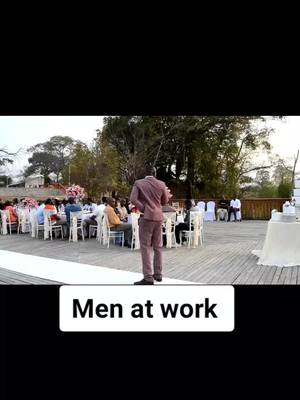 A man in a maroon suit stands with his back to the camera, addressing a seated audience in an outdoor setting. The scene is at a banquet or wedding, with tables, chairs, and trees in the background. The hook text is located at the bottom of the image in a white rectangle with a black border.