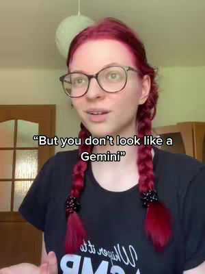 A young woman with bright red hair in two braids wearing glasses poses for the camera with text overlay. The background has a light fixture and glimpses of a room.