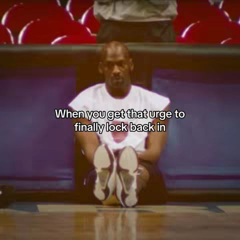 The cover image depicts Michael Jordan seated on a wooden floor in a basketball arena. He is wearing a white t-shirt and black shorts, with his legs extended and his shoes pointing towards the viewer. The background includes rows of red stadium seats and a blue barrier.