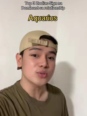 A young man wearing a tan baseball cap and an olive green shirt is positioned in the center of the frame, looking upwards towards the top left corner. Above him, white text reads, "Top 3 Zodiac Sign na Dominant sa relationship". Below this text, in large yellow text, the name "Aquarius" stands out. The background is a plain, off-white wall.