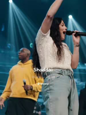 The cover image shows a live performance on stage, with a female singer in the foreground holding a microphone and singing with her right arm raised. Behind her to the left is a male figure with a microphone. Overlaid on the image is the word "Shaddai" with an audio waveform and a social handle @Winnie.