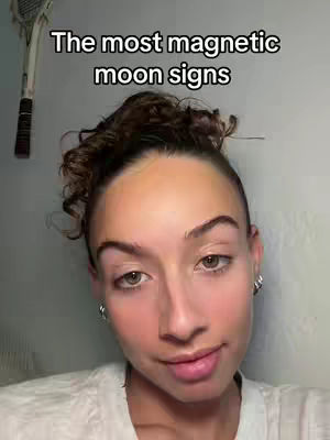 A close-up shot of a woman's face with text overlayed. She has light skin, dark hair pulled back in a bun, and small hoop earrings. The text reads, 'The most magnetic moon signs'. A tennis racket hangs in the background.