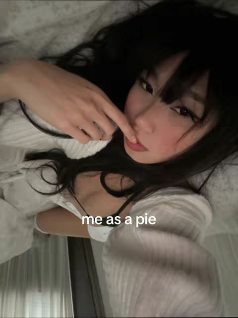 A selfie taken from a low angle shows a woman lying down. She has long, dark hair and is wearing a white top. Her finger is touching her nose, and the text 'me as a pie' is superimposed on the image.