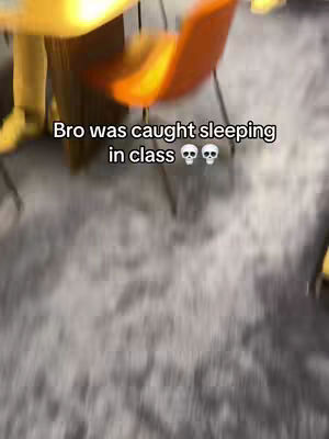 The video cover shows an out-of-focus interior scene. The floor of the room is gray, and at least one orange chair and a wooden table are visible. The text overlay reads, "Bro was caught sleeping in class 💀💀."