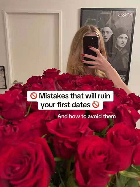 A woman with long blonde hair is taking a selfie in front of a large bouquet of red roses. She is holding a black phone, covering part of her face and the camera. The background includes a white door, a framed artwork and a partially visible window, creating a soft, natural lighting.