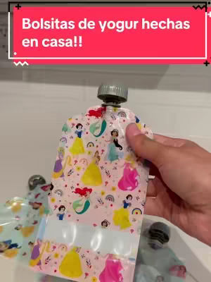 A hand holding a pouch filled with a yogurt. The pouch features a pink background with cartoon princess illustrations, like Snow White, Rapunzel, and Ariel. Additional pouches with similar content are in the background. A red banner at the top contains white text over a red background.