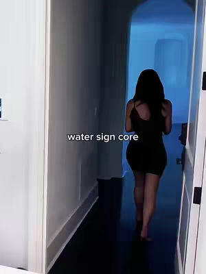 A woman in a black dress is shown from the back, walking away from the camera down a hallway. The hallway is lit, with a blue light emanating from a doorway at the end. The words "water sign core" are overlaid on the image.