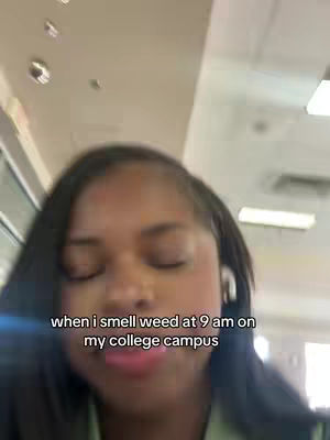 A selfie-style image showing a person with closed eyes, positioned in what appears to be a college setting. Text overlayed on the image indicates the person has detected the scent of marijuana on campus. The background includes architectural features.