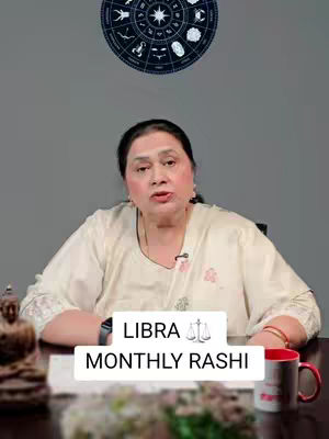 The cover image shows a woman sitting at a dark wooden table. Behind her is a dark gray wall with a circular zodiac chart displayed. In front of her is a white sign that reads "LIBRA" above an image of scales indicating the libra zodiac sign and "MONTHLY RASHI". A red and white mug is on the table along with a small decorative statue of a deity.