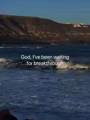 The image features a seascape with a clear blue sky overhead. The water is a dark blue, with visible waves rolling towards the shore. A mountain range or cliffs form the backdrop, and the overall feel is serene with a sense of vastness.