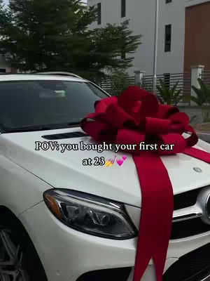 The cover image shows a white Mercedes-Benz car from a slightly high angle. A large red bow decorates the hood of the car. The text overlay reads '\"POV: you bought your first car at 23\"'.