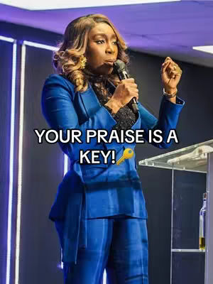 A woman in a striking blue suit stands on a stage, holding a microphone and addressing an audience. She has dark skin, styled hair, and is smiling. The background features sleek lighting design. Text overlay highlights the key message.