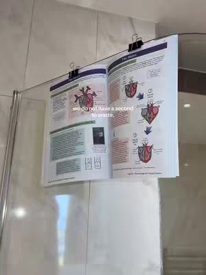 A book with anatomical diagrams is clipped to a shower screen. Text overlayed on the page reads, 'we do not have a second to waste.'