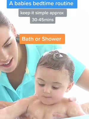 A woman is shown smiling and gently holding a baby boy who is fresh from a bath or shower. The baby is the focus, with water droplets in his hair and a calm expression. The woman is in the background with a turquoise shirt.