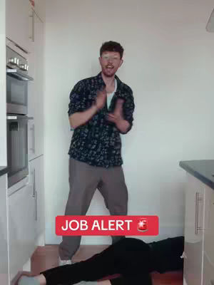 A man in a patterned shirt claps his hands enthusiastically in a kitchen, above a person on the floor. A red banner with white text reading 'JOB ALERT' and a can is also in the shot.