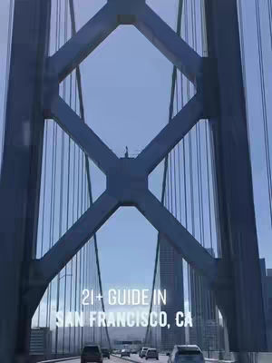 The image shows a view from inside a vehicle traveling over a bridge. The bridge's steel structure dominates the view, with the road and cityscape visible beneath. Text has been overlaid on the image.