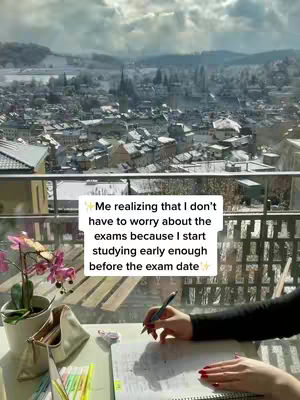 The cover image showcases a serene study scene. A woman's hands are visible, writing on a notebook with a pen. In the background, a stunning vista of a snowy town nestled amidst mountains is visible through a window. Beside the notebook on the desk are pens and a stylish pouch. A pot of flowers adds a touch of life to the composition. The text overlay reads: "Me realizing that I don't have to worry about the exams because I start studying early enough before the exam date ✨"
