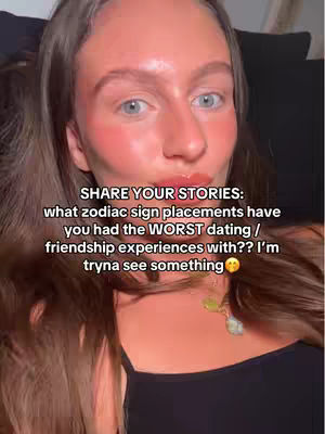 A close-up shot of a woman's face with a text overlay. The woman has light skin, rosy cheeks, and reddish-pink lips. Her eyes are blue. Her dark brown hair is styled down to her shoulders. She is wearing a black top and a pendant necklace with a green gem. The text overlay has white text on a dark background.
