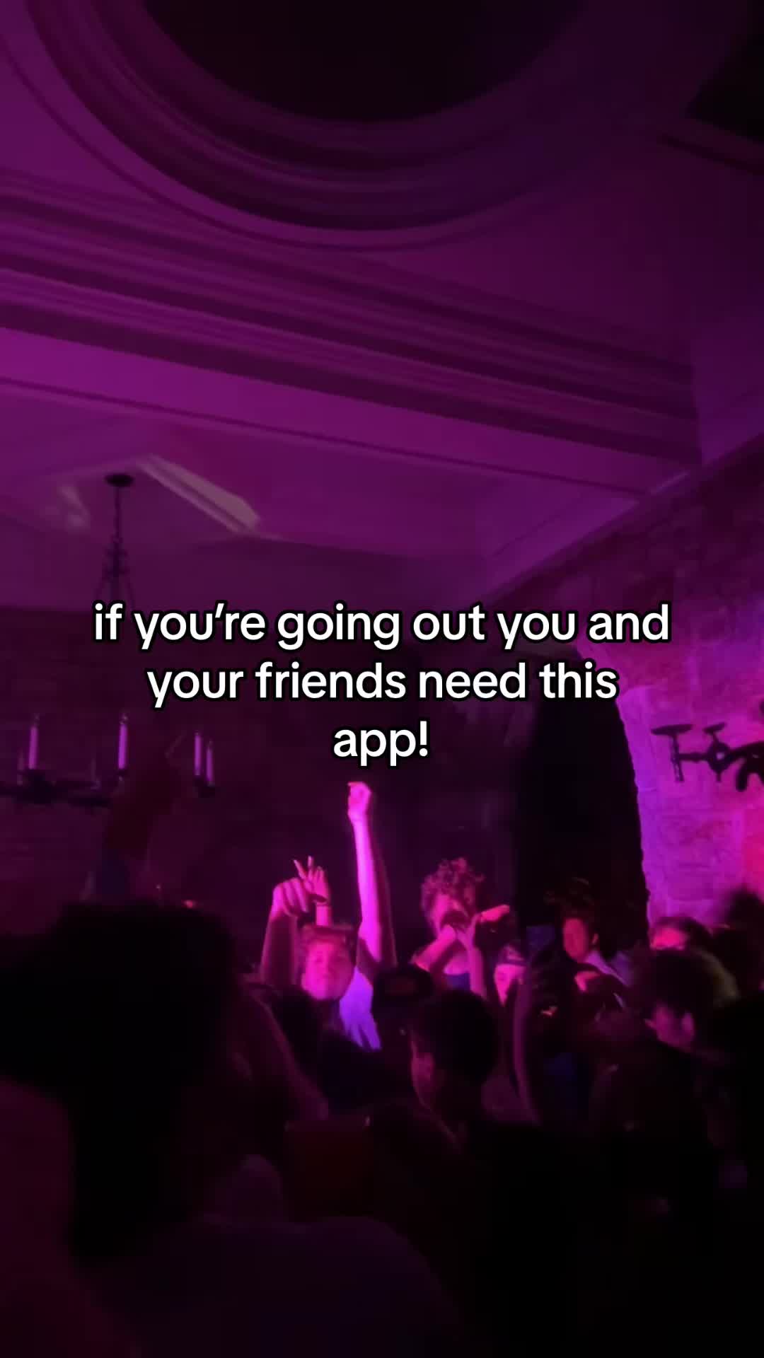 The image captures a vibrant nightlife scene inside a venue, likely a club or bar, illuminated with purple lighting. The foreground is filled with a crowd of people with raised arms, some holding phones, suggesting a lively atmosphere. The text overlay reads, "if you're going out you and your friends need this app!"