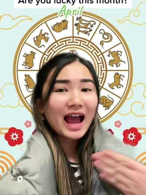 A young woman with dark hair and open mouth smiling into the camera while pointing with her right hand. Behind her is a background featuring a Chinese zodiac wheel and red flower ornaments with a light sky-blue background.