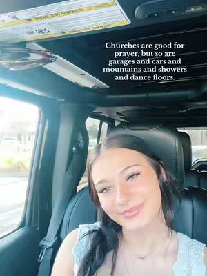 A young woman is inside of a car, with a text overlay on the top right corner. The text conveys the idea of prayer being available in any environment.